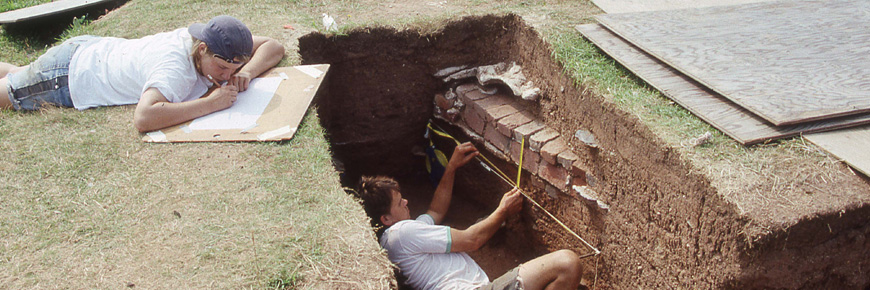 Two people working excavating artifacts in the ground at Fort Charles.