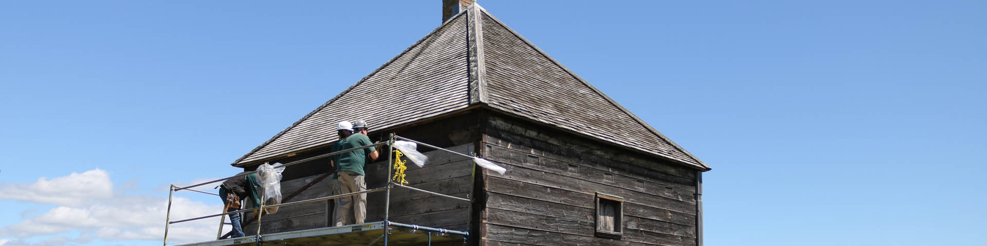 Parks Canada staff work on the Fort Edward NHS blockhouse, which is surrounded by scaffolding and fencing.