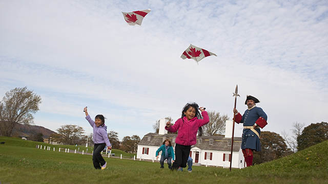 A costumed interpreter watches two young girls fly kites on the grounds at Fort Anne National Historic Site.