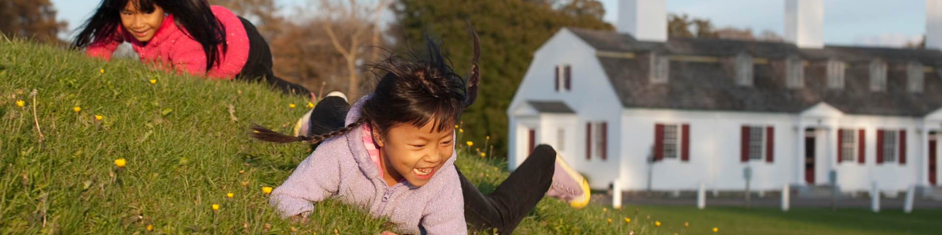 Two girls laughing and rolling down a hill while enjoying the defensive banks, ditches, and bastions at Fort Anne National Historic Site.