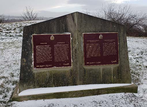 A snowy stone monument with two maroon plaques.