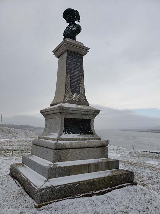 A tall stone monument with a bust of Pierre Dugua on the top, with the Annapolis River in the background.