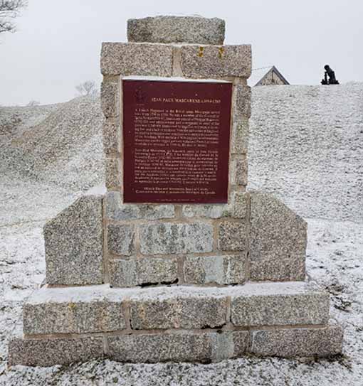 A snowy monument made of stone with a maroon plaque.