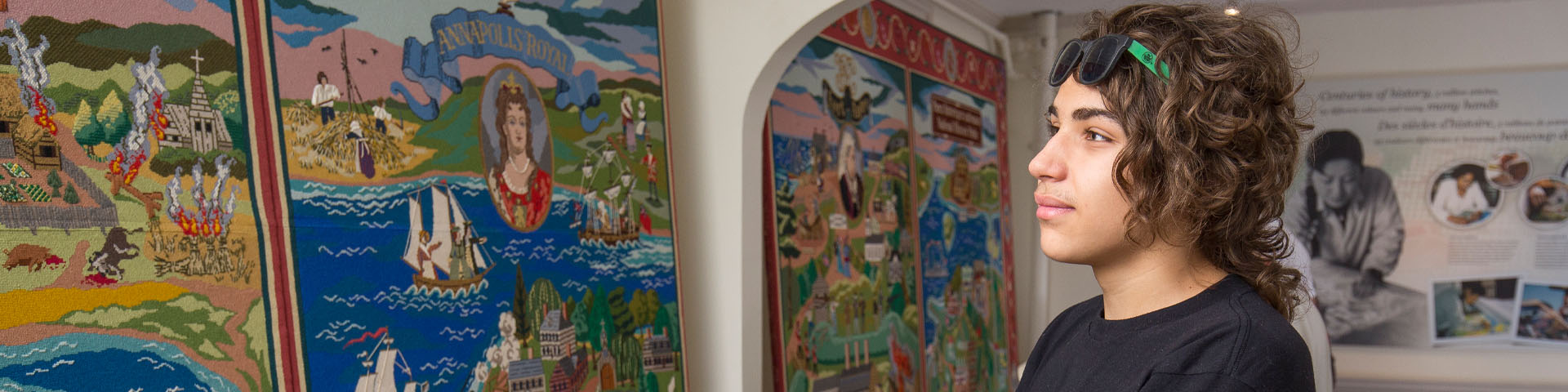Un jeune visiteur admire la grande tapisserie historique colorée qui recouvre un mur au lieu historique national du Fort-Anne. 