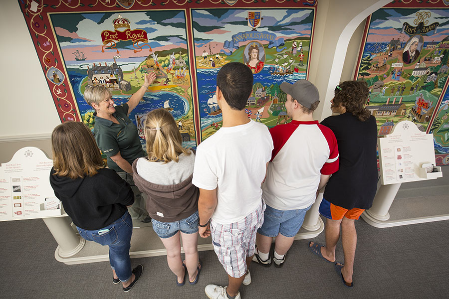 Visitors listen to a Parks Canada tour guide explaining the large and colourful heritage tapestry covering the wall.