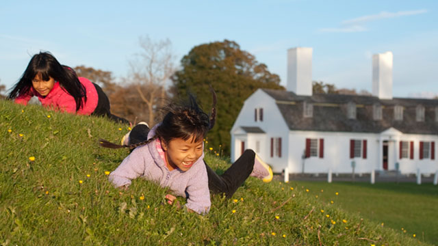 Two children rolling down the grassy walls of the fort. 