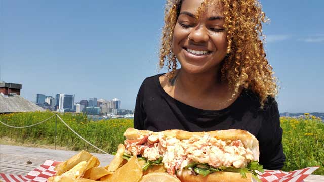 Une visiteuse mange un petit pain farci au homard et des frites. 