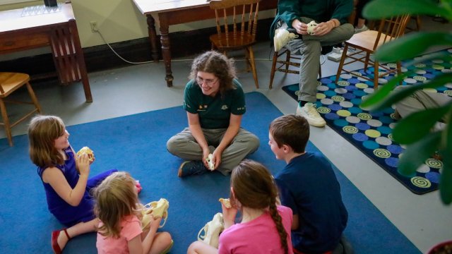 Dans le cadre d'un programme de sensibilisation, les élèves s'assoient sur le sol avec un employé de Parcs Canada et tiennent des objets dans leurs mains.