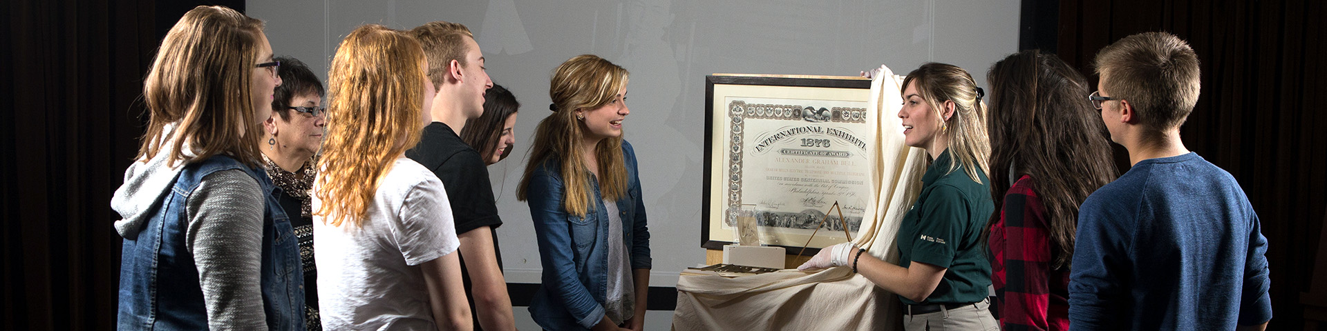 A group of visitors stand around an artifact that is being unveiled by a uniformed Parks Canada interpreter 