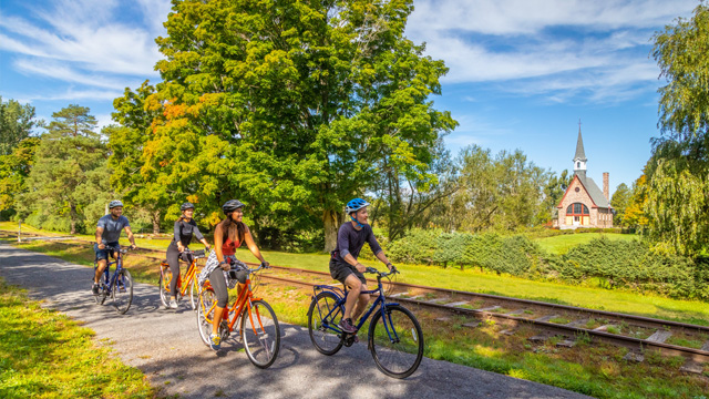 Four cyclists on the Harvest Moon Trail with a view of the Grand-Pré Memorial Church in the background.