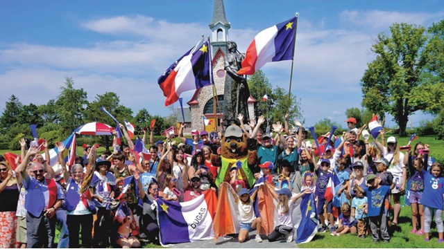 A large gathering of people in front of the Memorial Church in Grand-Pré, with flags and clothing of Acadian colours.