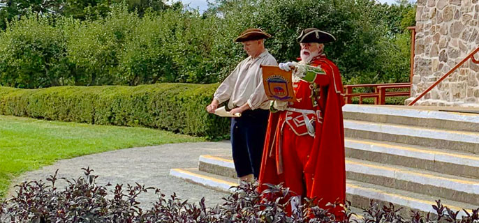 Two costumed interpreters reading a document in front of the Memorial Church at Grand-Pré