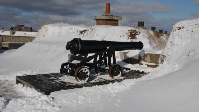 A large black cannon on wheels surrounded by snow.
