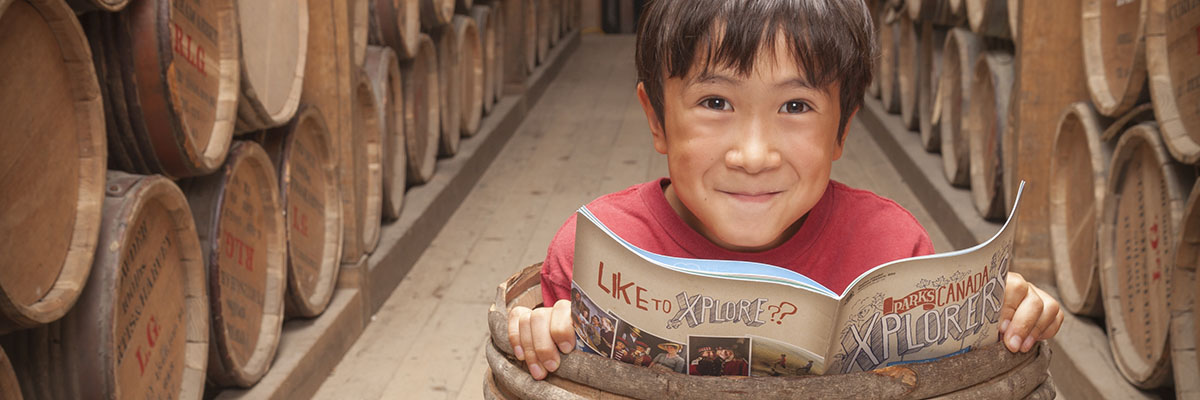 A child stands inside a barrel in the powder magazine, smiling and looking up from an explorer booklet at Halifax Citadel National Historic Site.