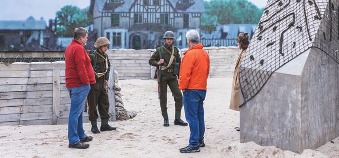 Two visitors and two soldiers stand among the barricades from the “Storm the Beach