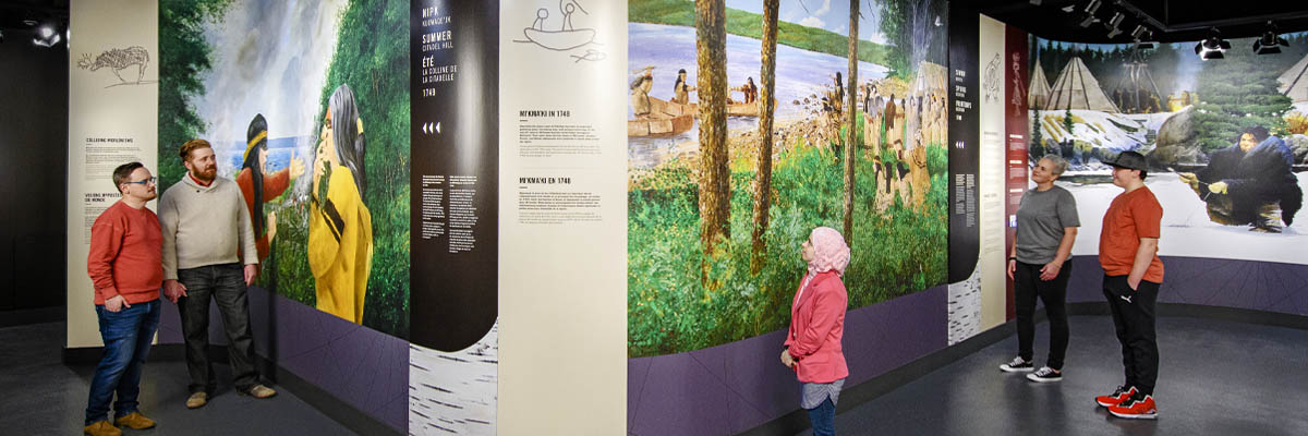 Masked visitors looking at large floor to ceiling panels of Mi’kmaq art.