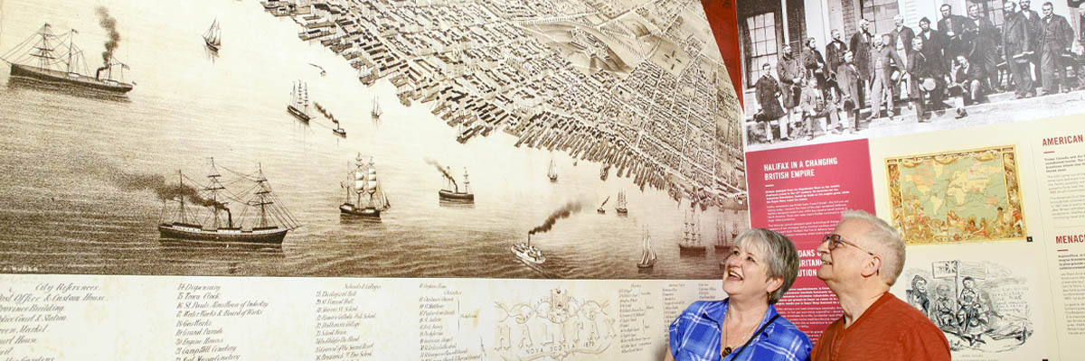 Visitors pointing at a large floor-to-ceiling historic map of Halifax