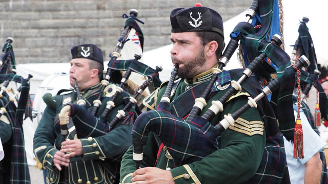 Two soldiers in green uniforms playing bagpipes.