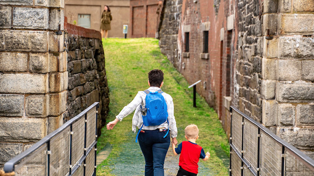 A parent and child cross a footbridge into the fort.