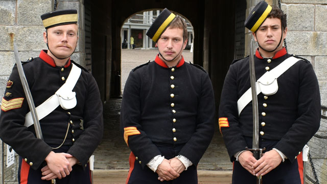 Three people in dark blue uniforms with brass buttons and pillbox hats.
