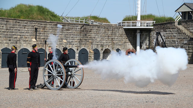 Soldiers in blue fire a small cannon on wheels in the Parade Square.