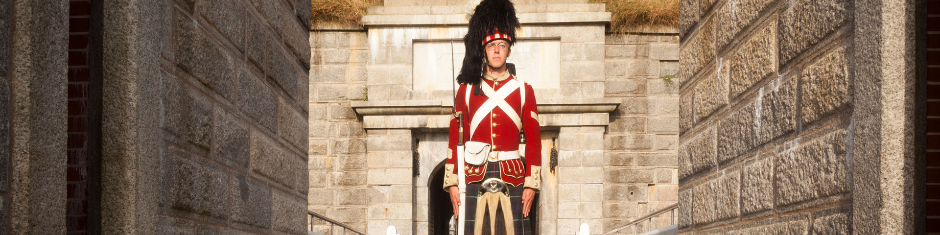 Un soldat en uniforme complet du 78e régiment des Highlanders tient une carabine près des murailles. 