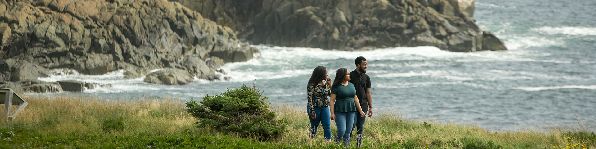 Trois personnes marchent le long du littoral avec l'océan et de grands rochers en arrière-plan.