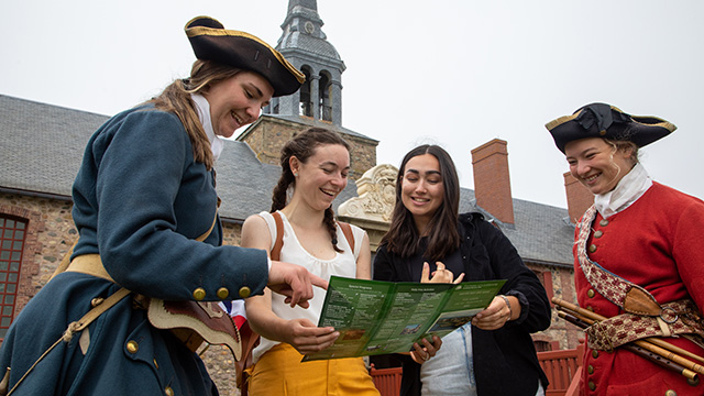 Two women read a brochure with two costumed interpreters