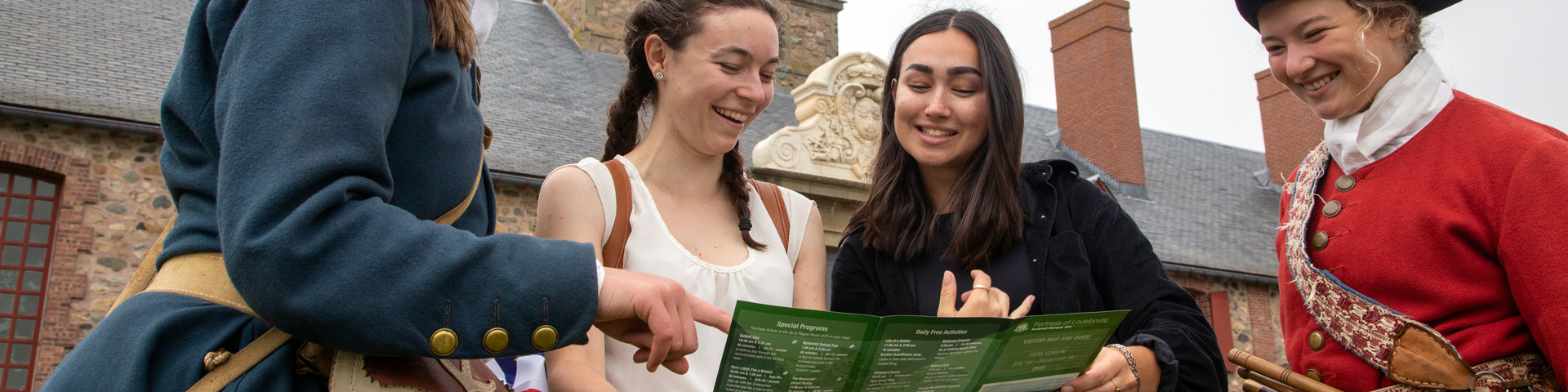 deux visiteurs consultent une brochure en compagnie de deux interprètes en costume d'époque