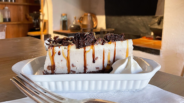 A chocolate and caramel covered cheesecake in a white ramekin