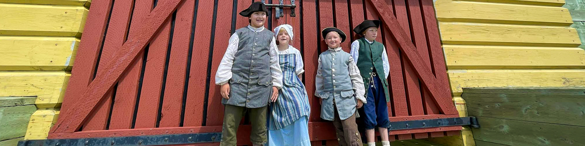 Quatre enfants debout devant un grand portail en bois rouge.