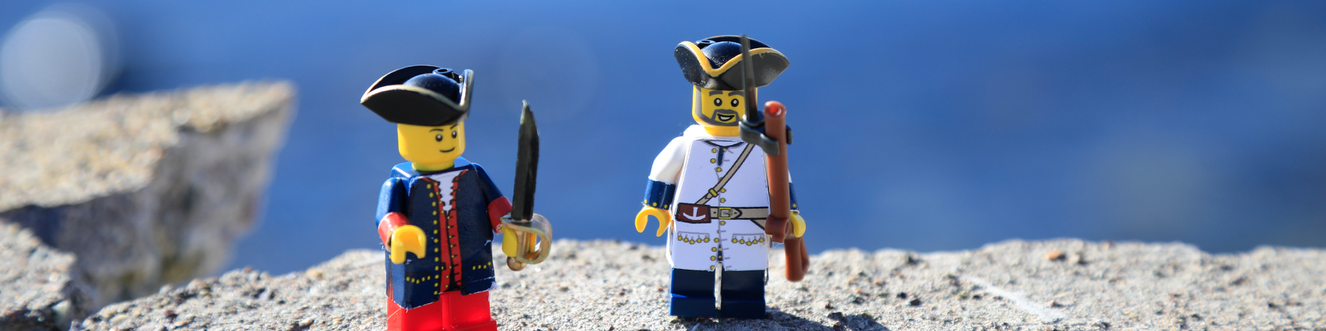 Two lego figurines standing on a rock with the ocean behind them.