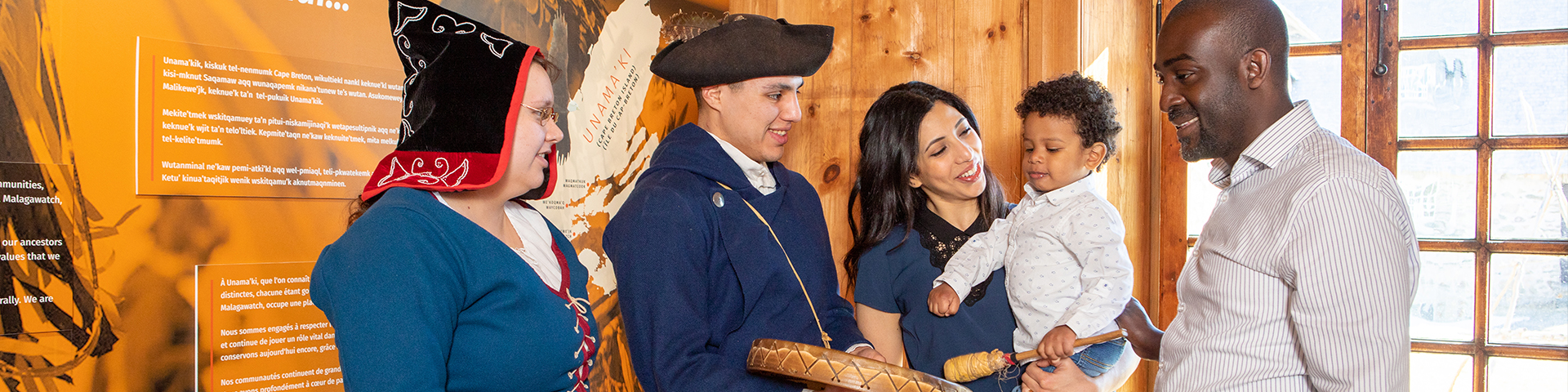 Two Mi'kmaq interpreters, one holding a drum, engaging with two adults and a child.