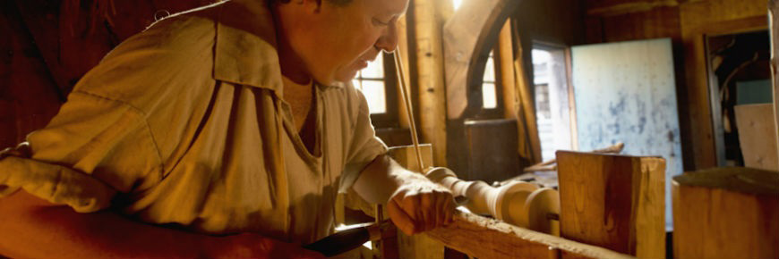 Craftsman in costume turning wood on a lathe