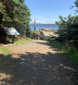 Large sentier de pierres et de terre menant à une structure en briques et au rivage.