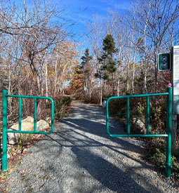Chemin en pierre concassée traversant un étroit portail métallique.