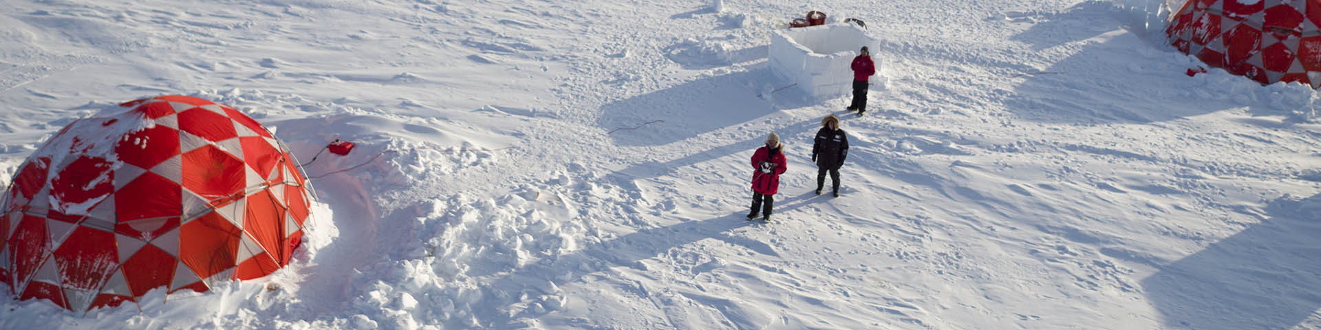 Une vue aérienne de trois personnes debout près de tentes dans la neige.