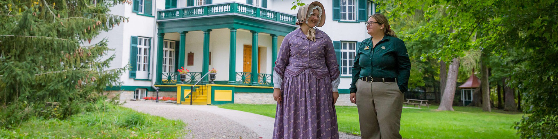 Two staff members stand in front of a historic house.