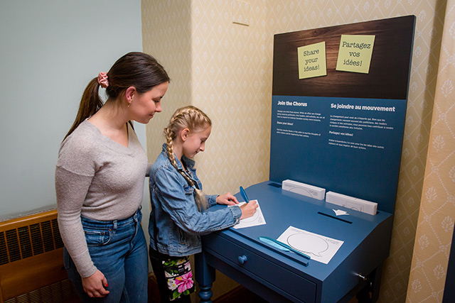 A women and girl write on a piece of paper at on an exhibit.
