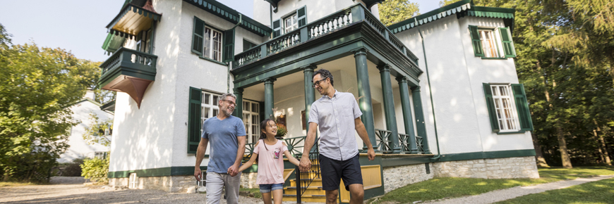 A family holds hands in front of a historic house.