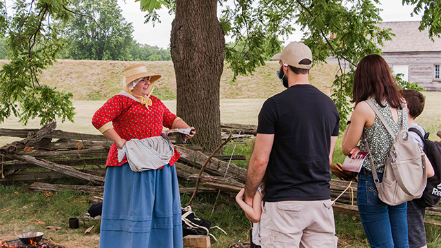 Heritage presenter in War of 1812 soldier's wife historic dress speaking to visitors