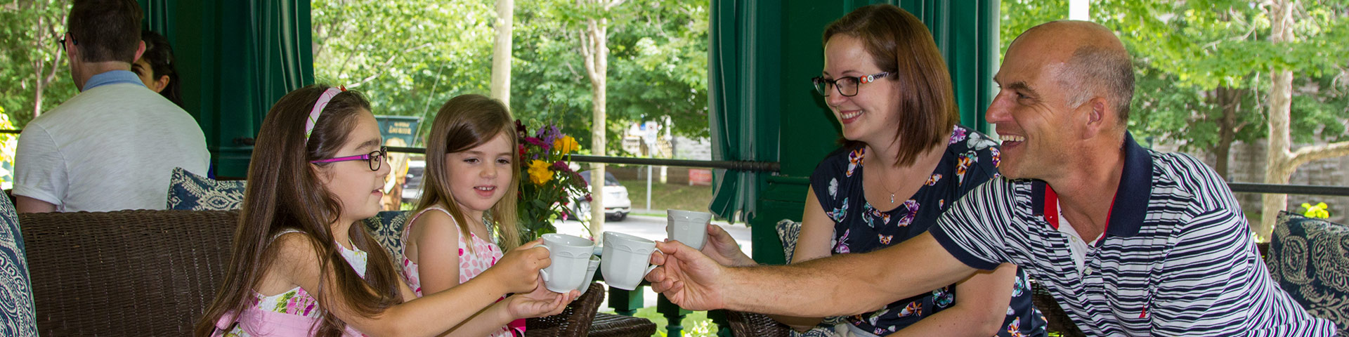 A family drinks tea on a historic verandah.