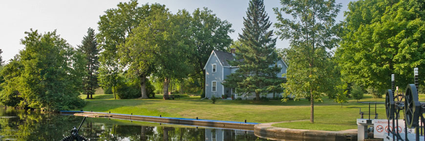 Plan large d’une demeure historique de couleur bleu ciel nichée entre plusieurs arbres d’un beau vert tout près du canal
