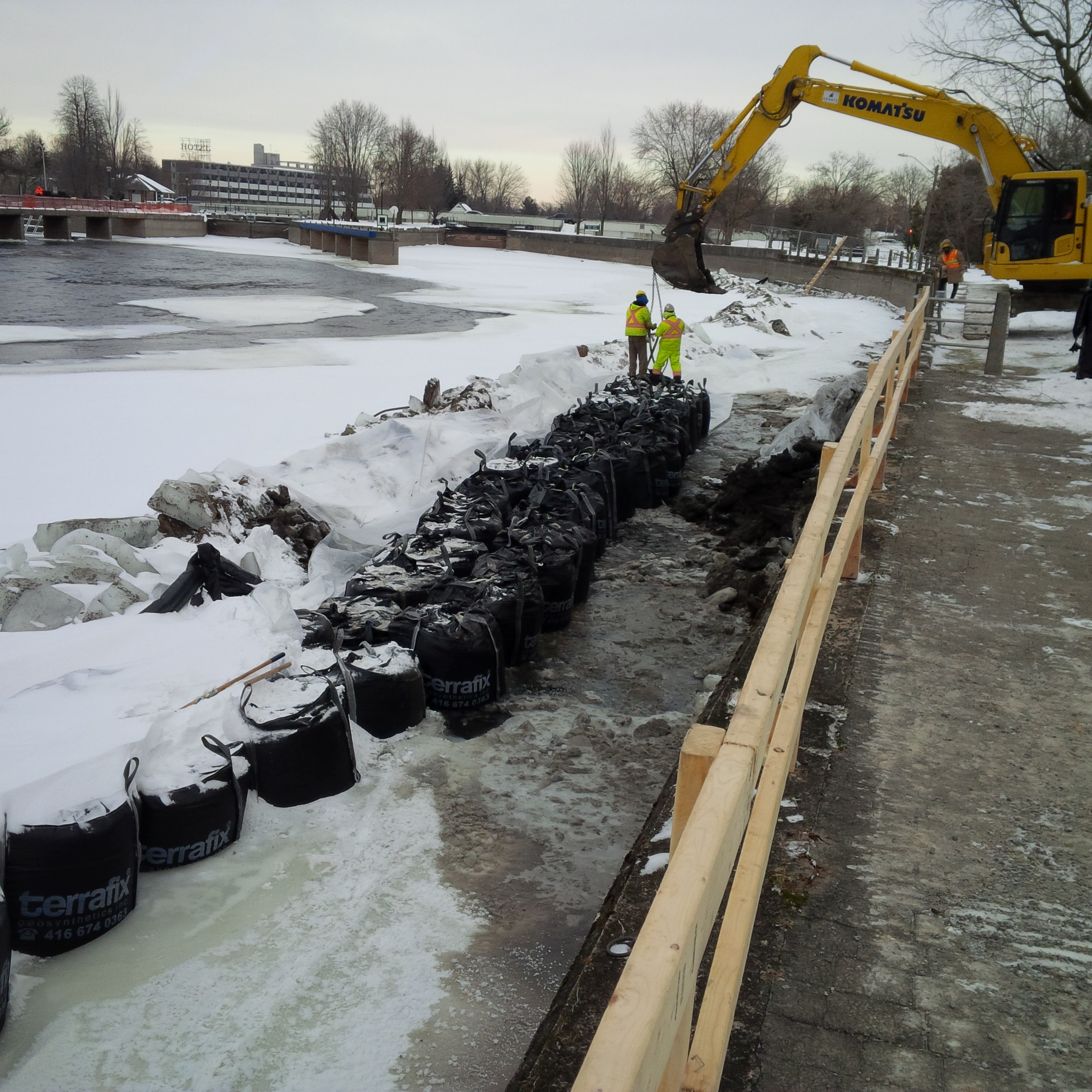 Workers untie components of the cofferdam from the bucket of an excavator – black metre bags filled with clean stone