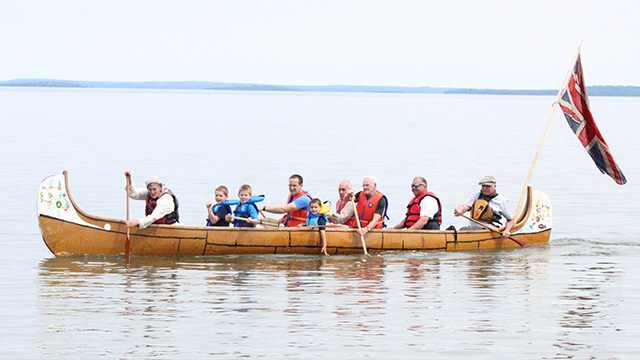 Un grand canoë rempli d'adultes et d'enfants pagayant sur un lac.