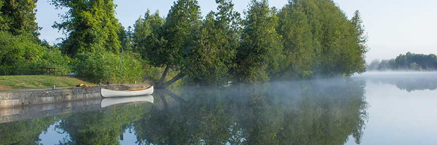 A canoe is moored at a lock on a foggy morning.