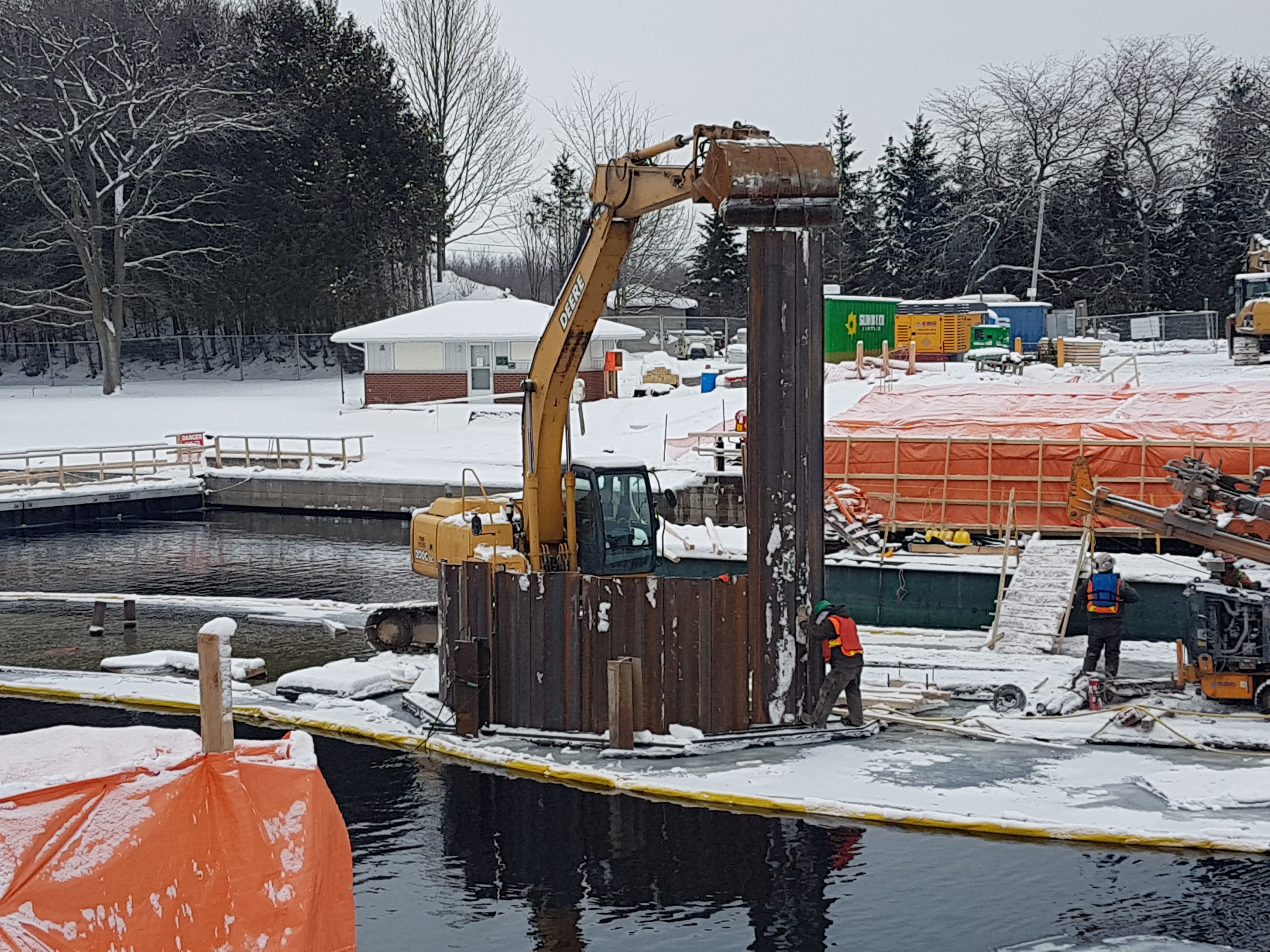 An excavator lifts forms into place at a snowy construction site.