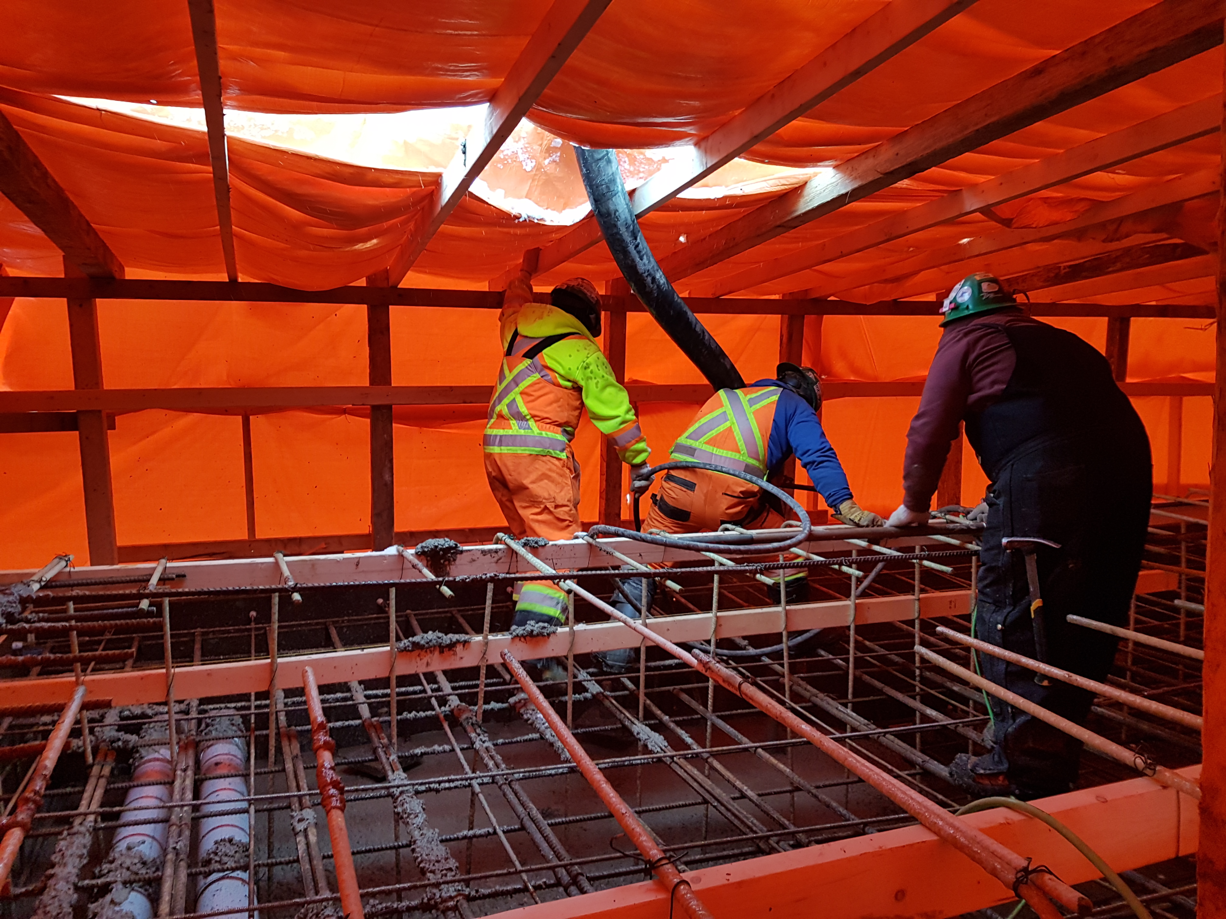 Men work under an orange tarp.