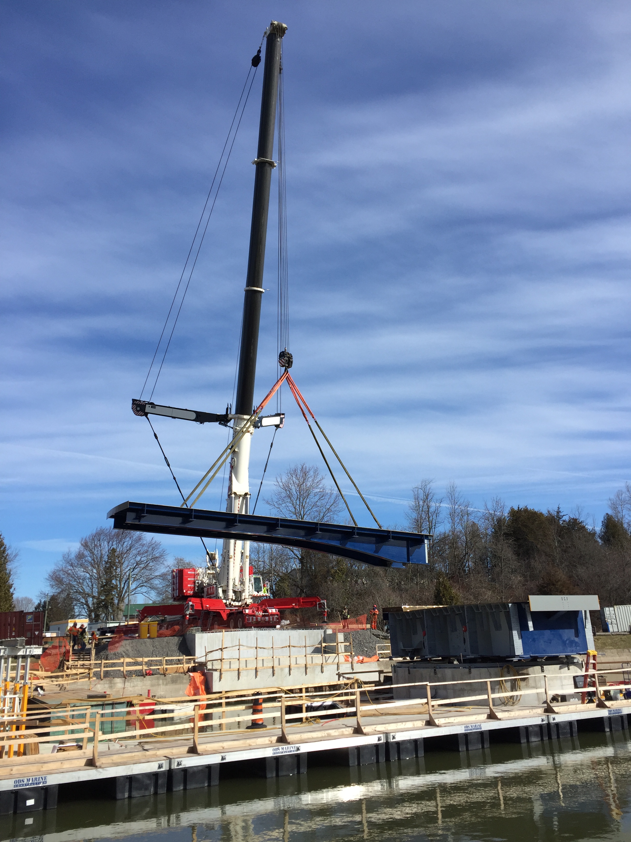 A large crane lifts a blue steel bridge