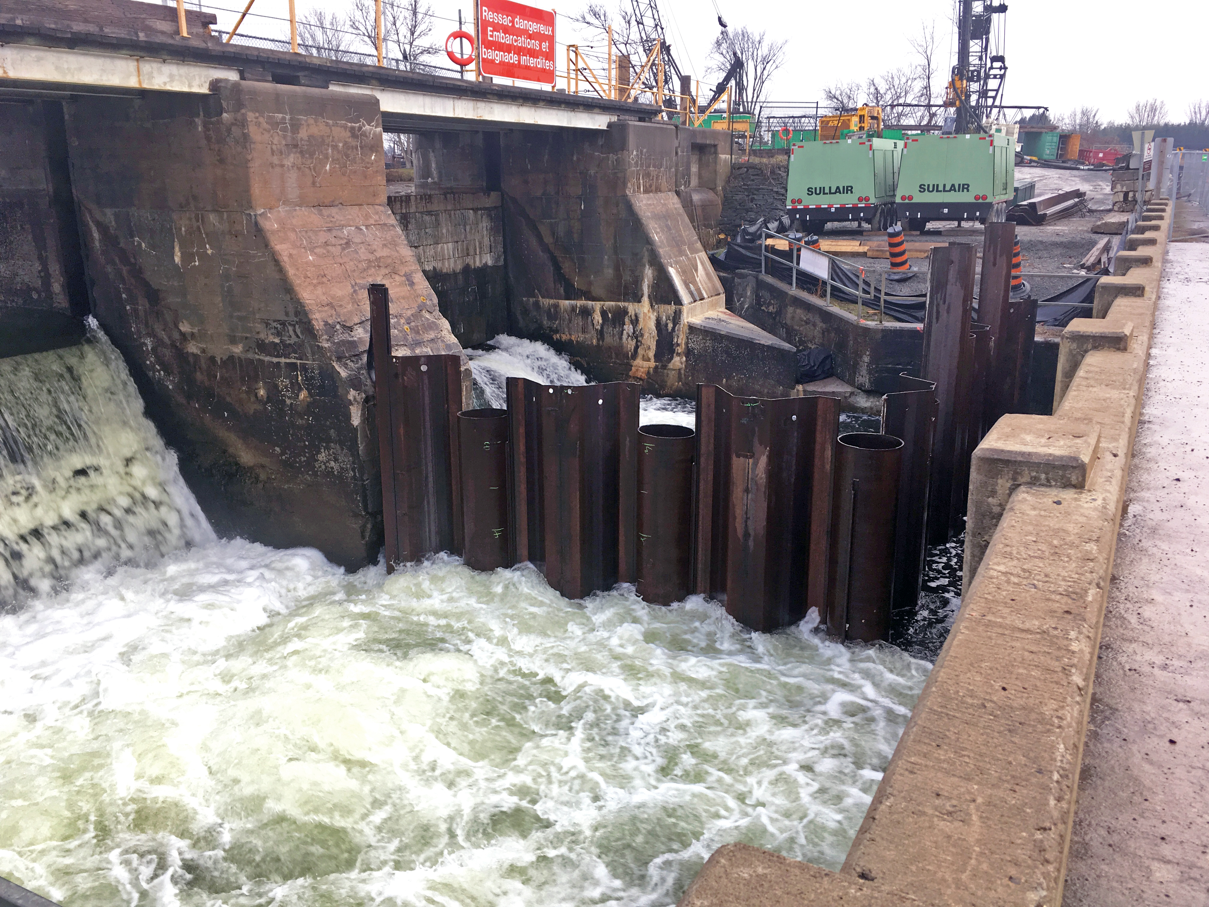 The outflow of two concrete dam sluices. Corrugated sheet pile surrounds the bottom of the right hand sluice in a square shape